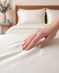 Hand touching soft white bedding on a bed with a wooden headboard.
