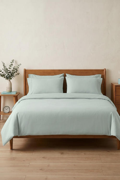 Bed with light blue bedding and wooden headboard in a room with Serene Green color scheme.